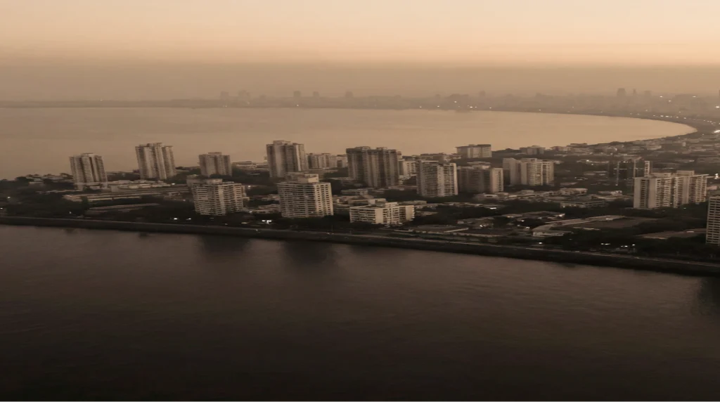 The Mumbai shoreline at dusk, the bay curving away past the headland.